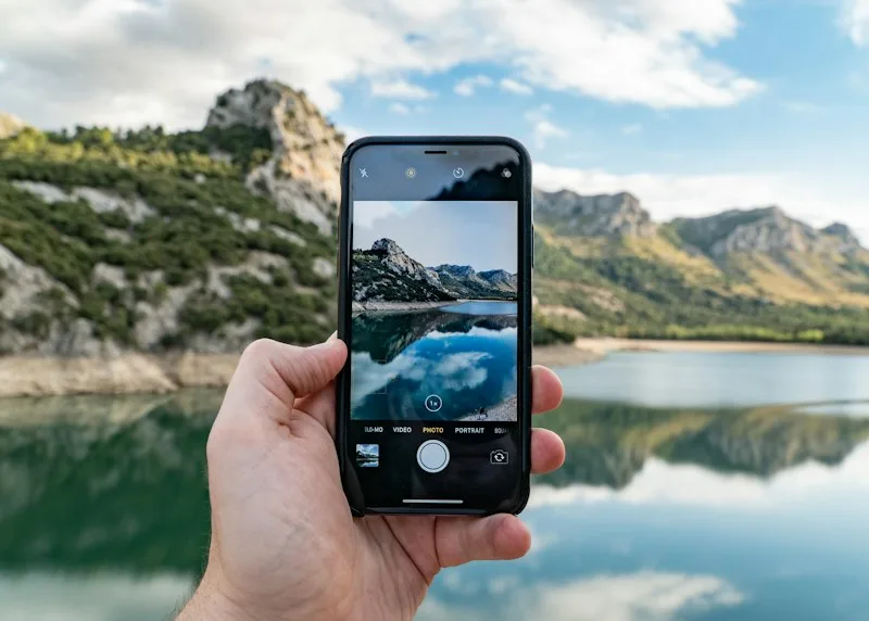 A traveller photographing a mountain lake on their phone, the place on screen and in front of them